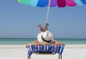 woman laying on a beach chair with legs folded in the air under an umbrella