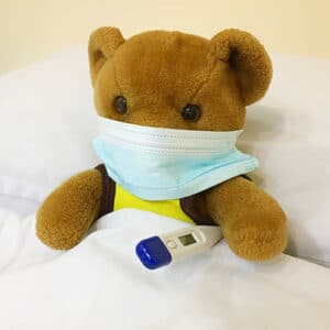 Teddy Bear in a hospital bed wearing a medical mask holding an electric thermometer