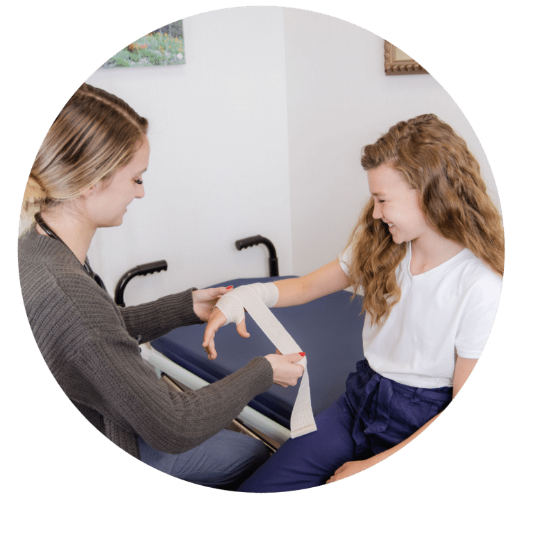 Female medical professional applying medical wrapping to a young girl's hand and arm.